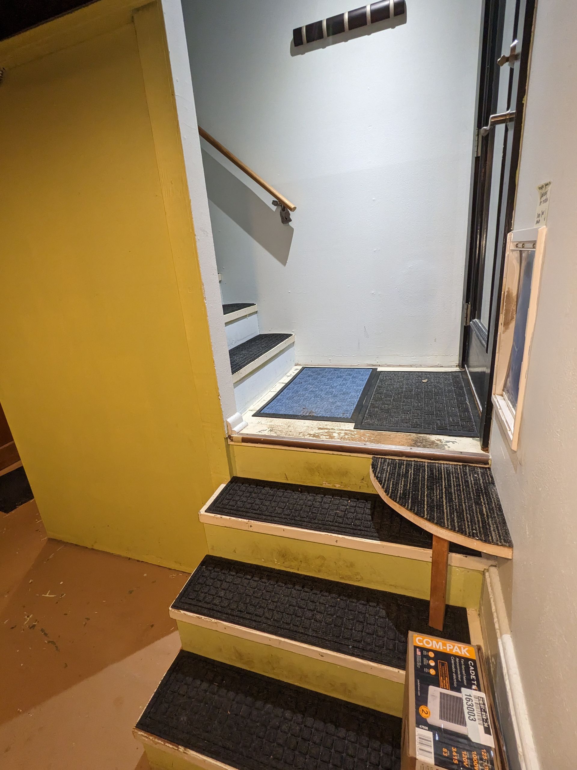 Indoor stairway with yellow wall, black steps, and a small rug at the landing.