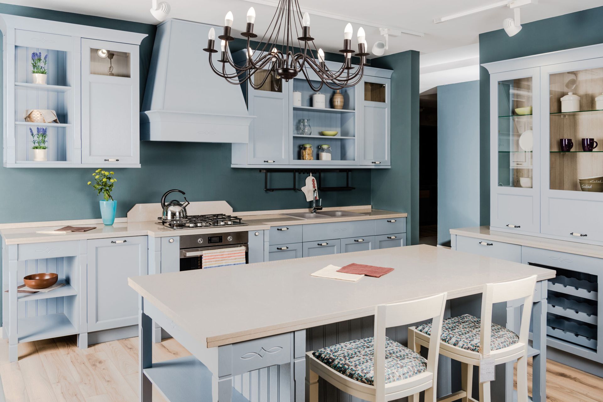 Bright modern kitchen with blue cabinets, white island, chandelier, and chairs around a dining table
