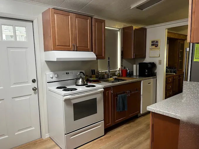 Small kitchen with white stove, wooden cabinets, sink, and countertop under warm lighting