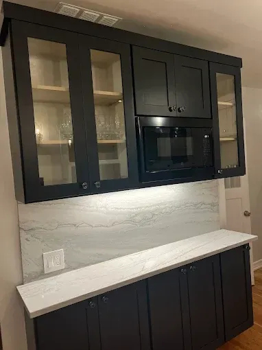 Black kitchen cabinets with glass fronts and built-in microwave above a white countertop.