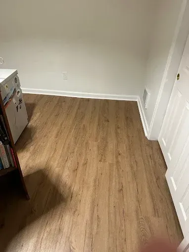 Empty beige room with wood flooring, white walls, and a closet door on the right.