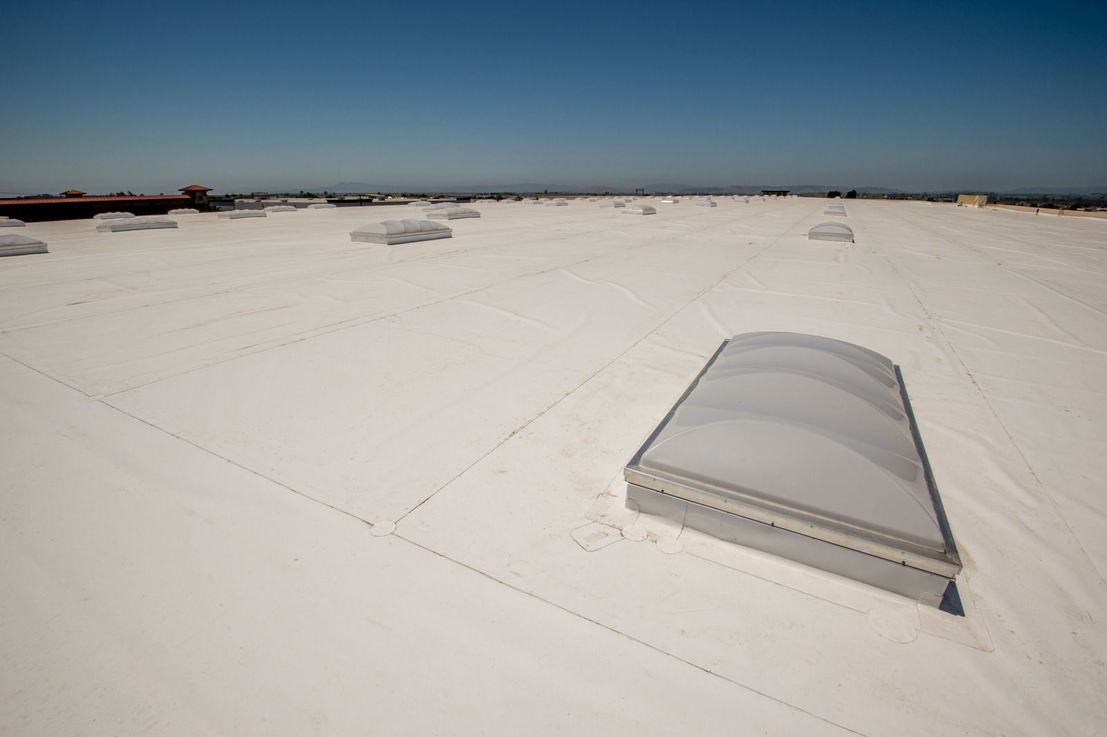 Wide rooftop with white surface and a translucent skylight under a clear blue sky.