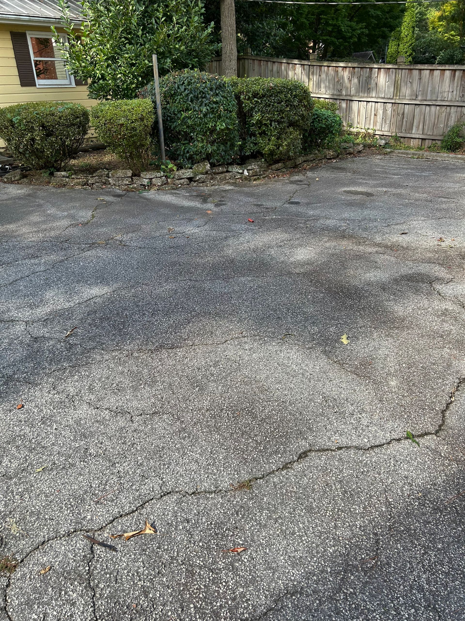 Cracked asphalt driveway beside a stone wall and shrubs near a house entrance