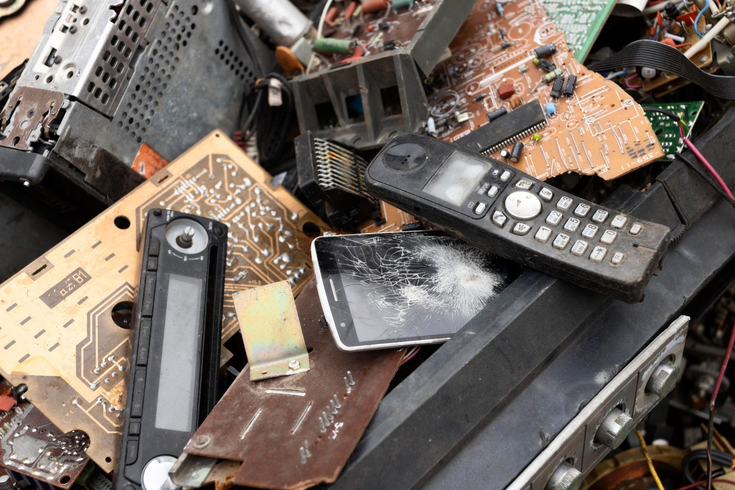 Pile of broken electronics including a shattered smartphone old cordless telephone and exposed circuit boards requiring professional electronic waste removal in Smyrna GA