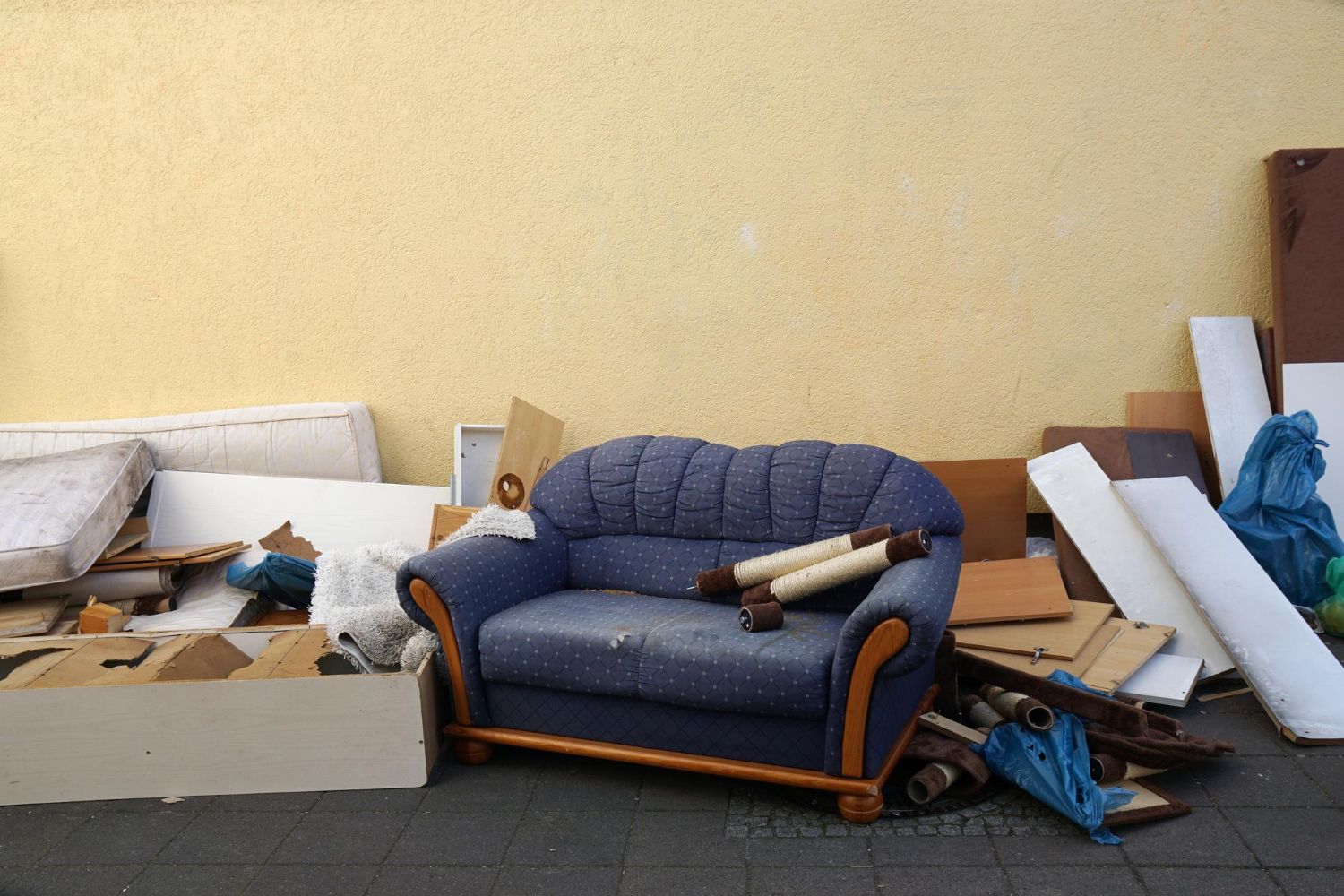 Old blue sofa and discarded household furniture piled outdoors for junk removal and trash hauling.