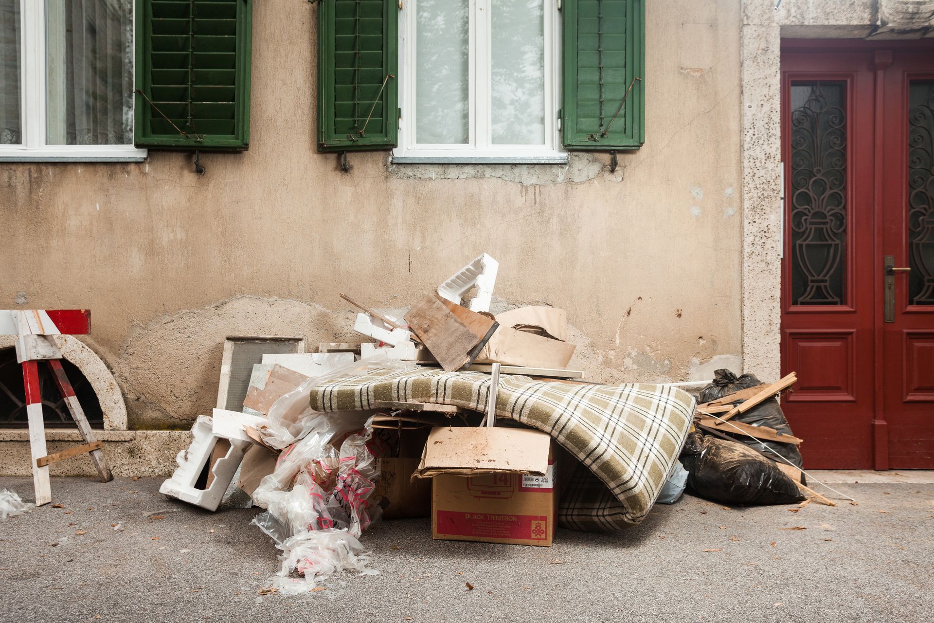 Large pile of bulk household junk featuring a plaid mattress cardboard boxes and styrofoam outside a residential building awaiting property clean out services in Smyrna GA