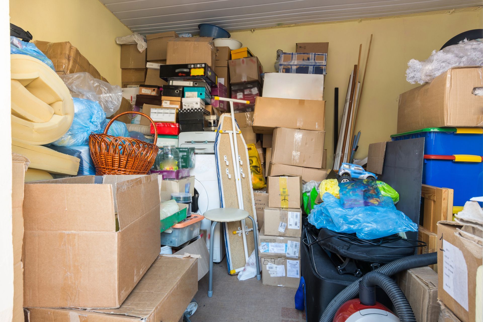 Overcrowded storage unit crammed full of stacked cardboard boxes household items an ironing board and plastic bins needing storage unit cleanouts in Smyrna GA