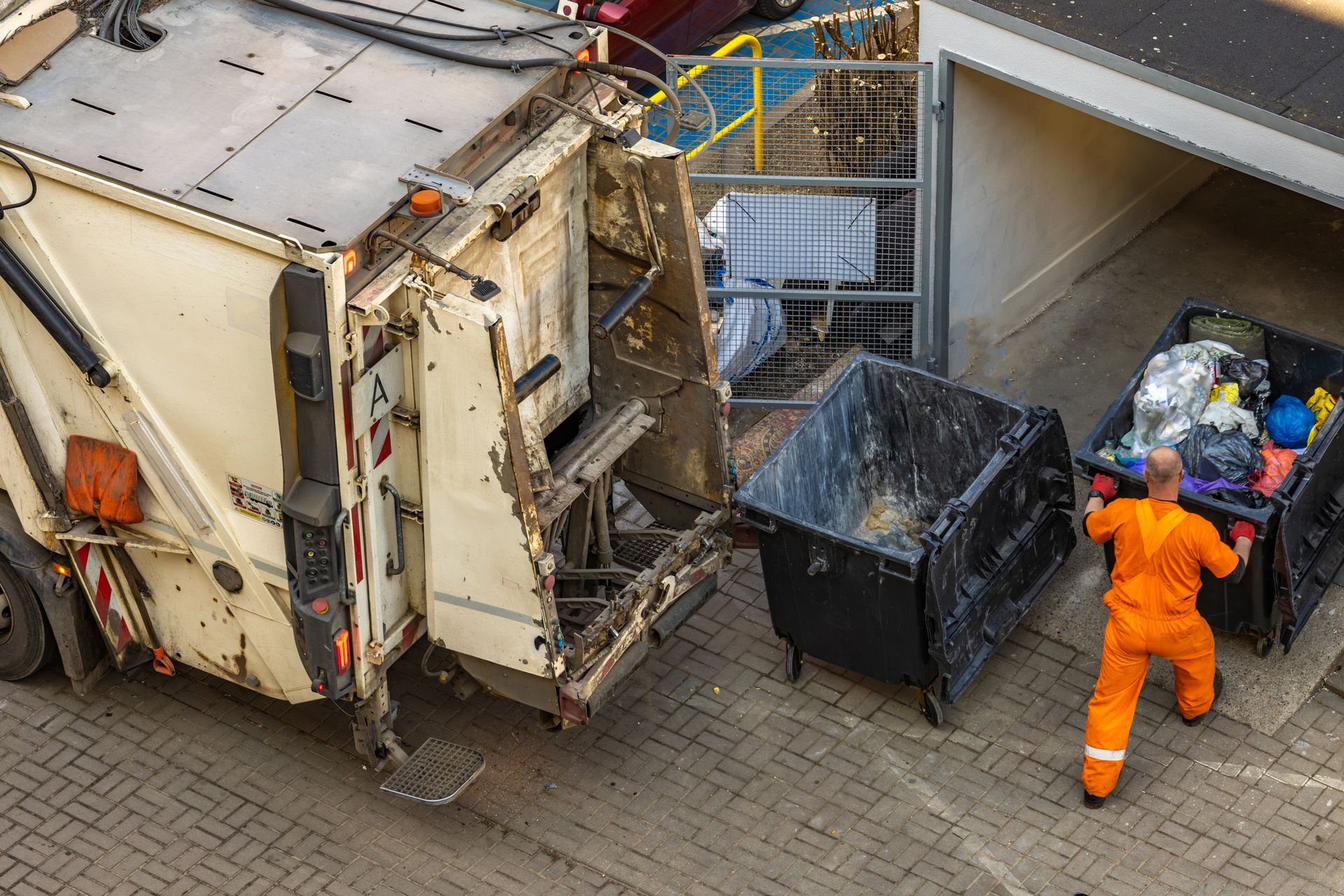 A sanitation worker in an orange uniform loading a large black commercial trash bin into the back of a garbage truck for professional waste management in Smyrna GA
