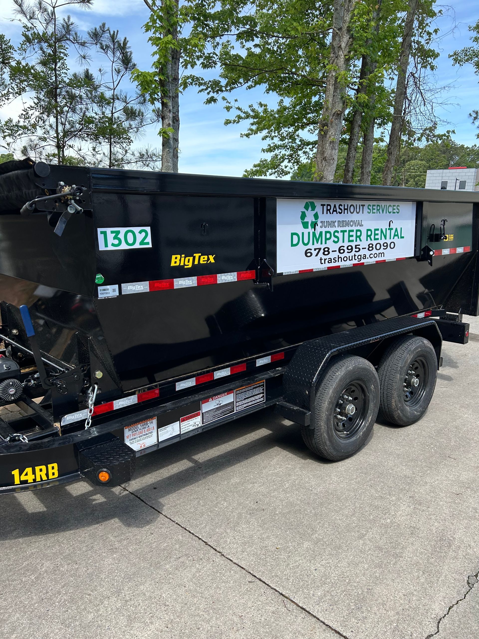 Black dump trailer with company decals parked on a road beside trees