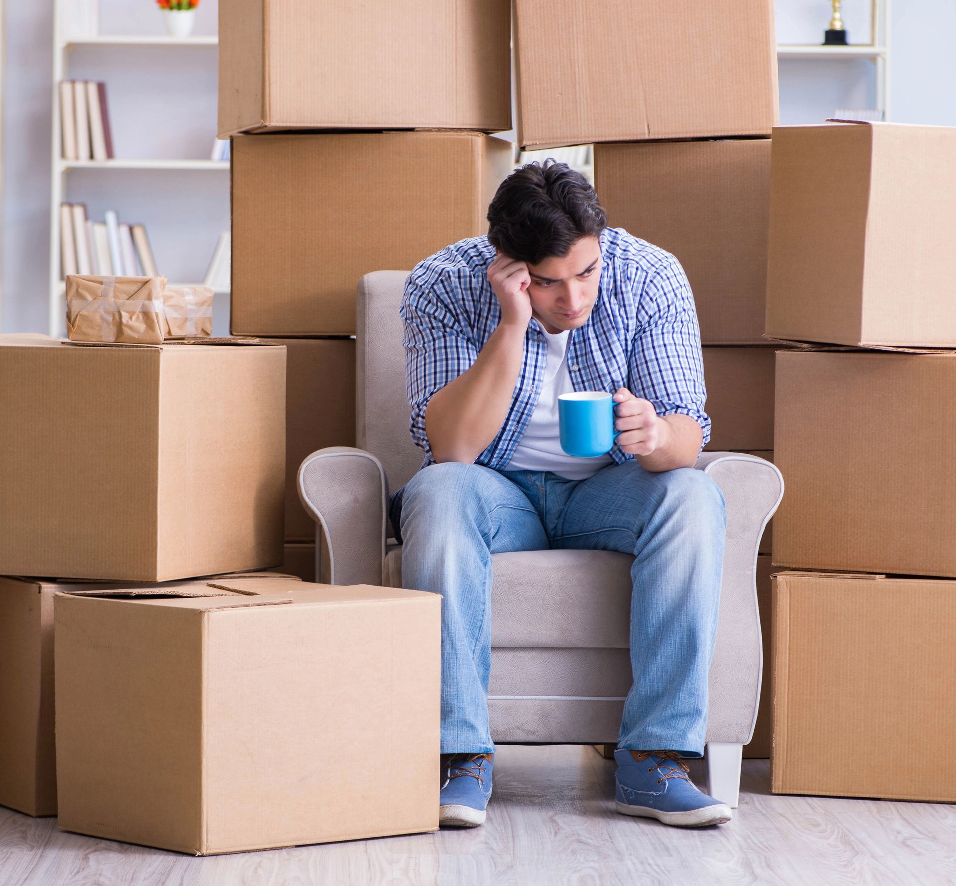 Stressed man holding a coffee cup sitting in an armchair surrounded by stacked cardboard boxes during a residential move in Smyrna GA