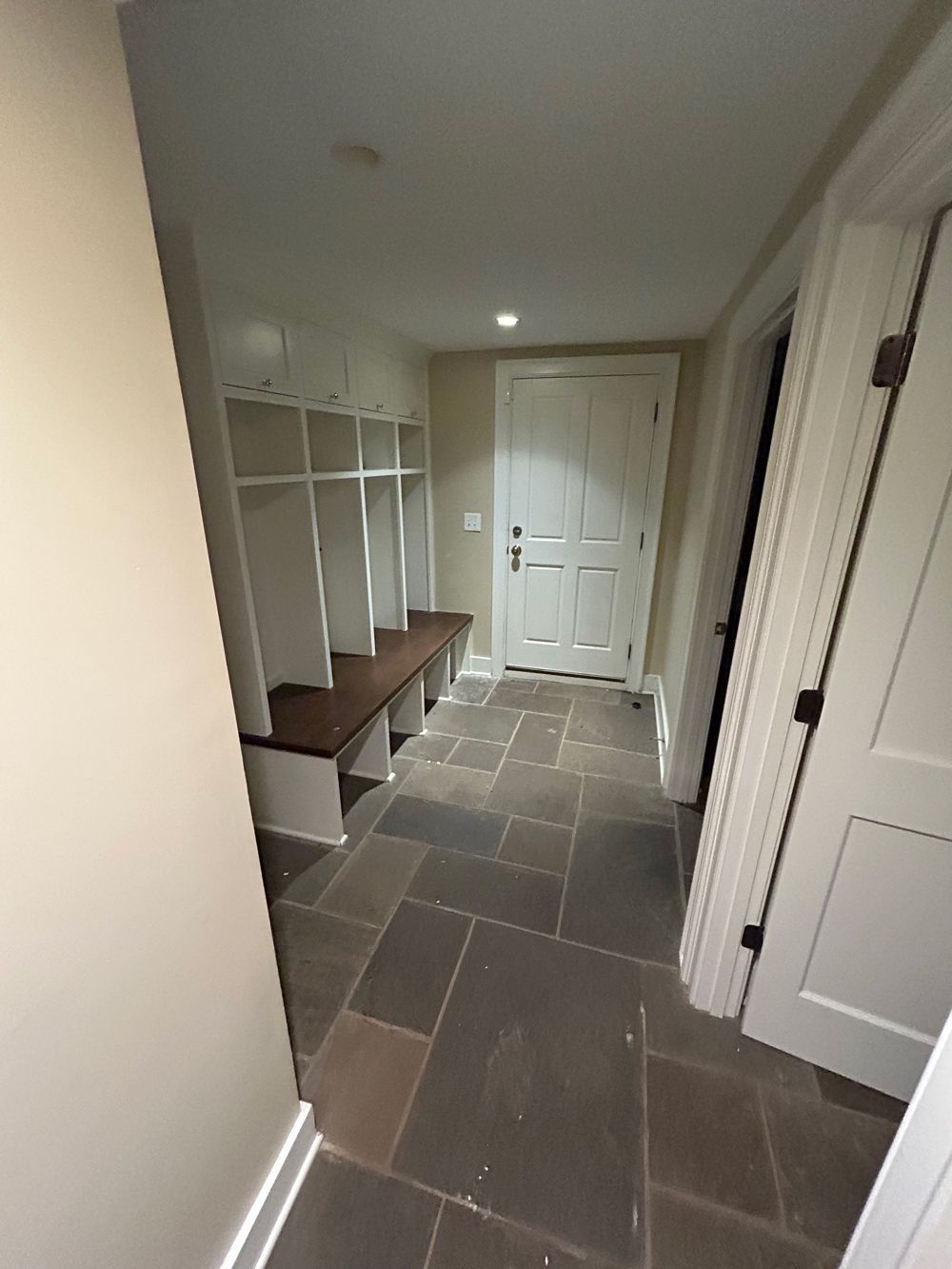 Narrow hallway with tiled floor, built-in cubbies, and white doors leading to a front entry.