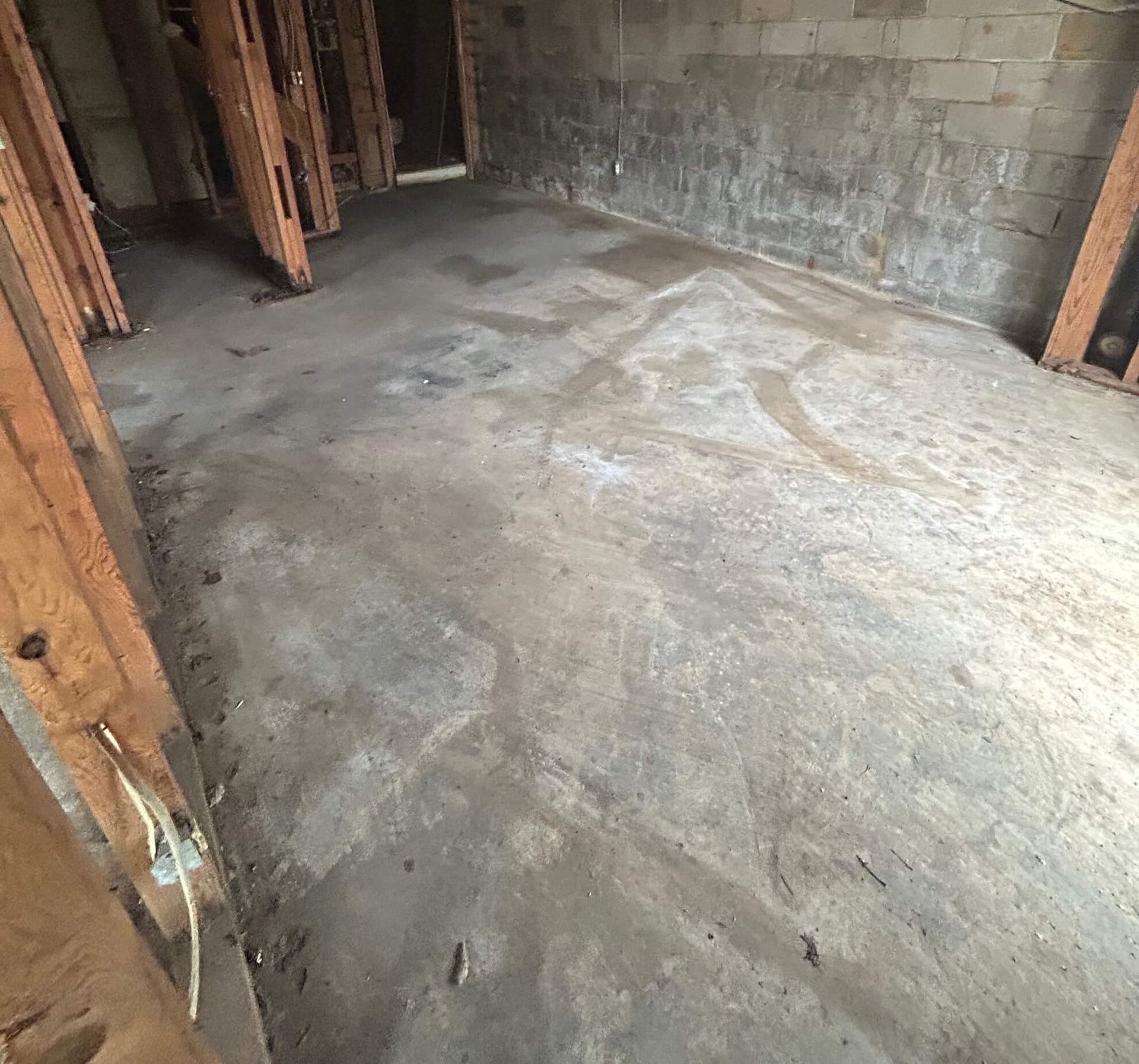 Bare concrete room under construction with exposed wooden framing and unfinished walls.