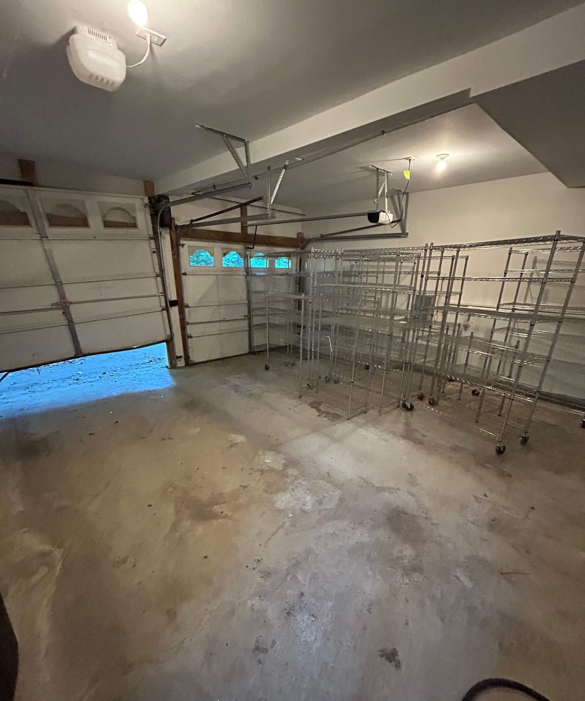 Empty garage with concrete floor, open garage doors, and stacked metal shelving along the right wall.