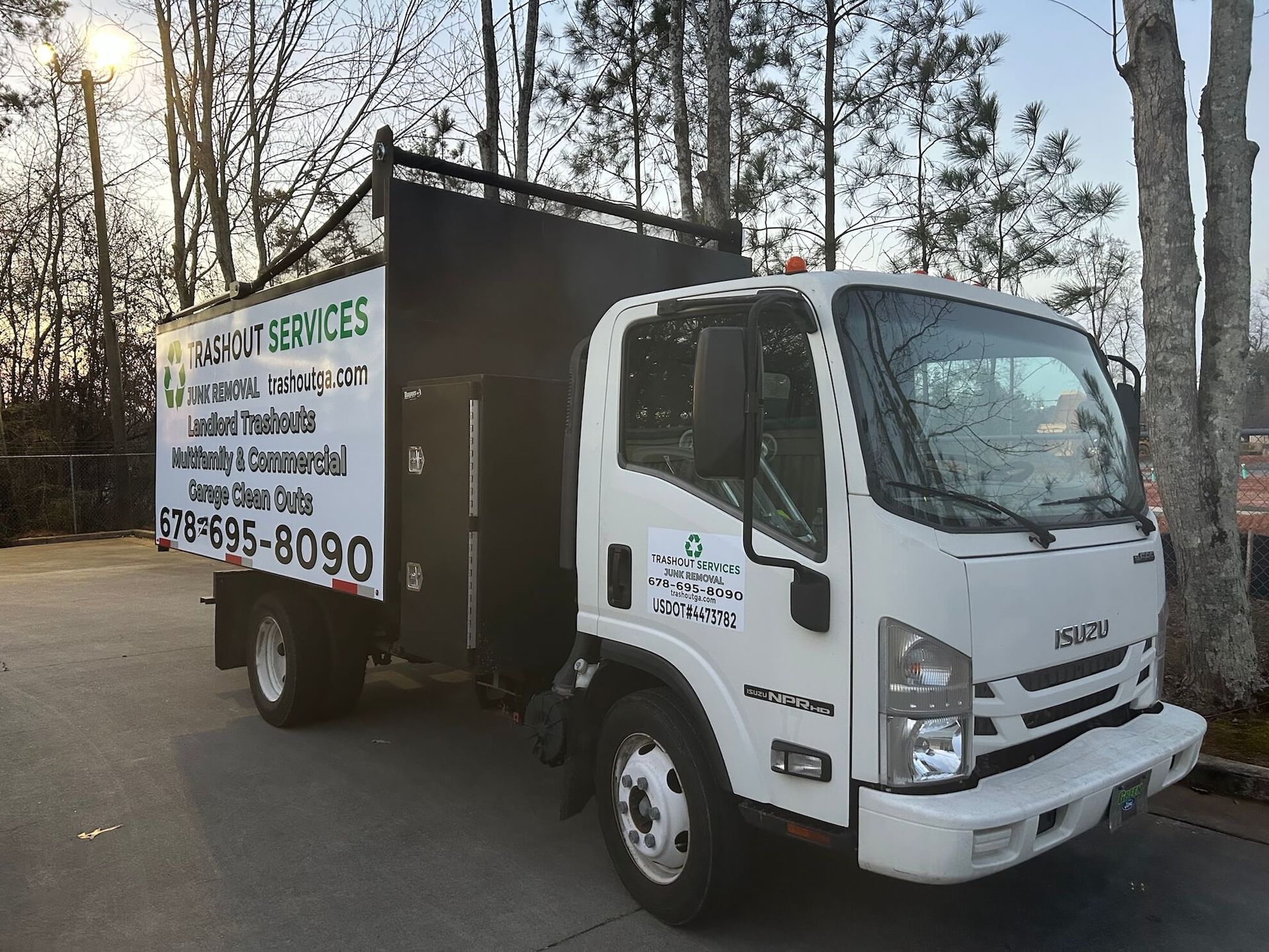White box truck with company signage parked on a road near trees