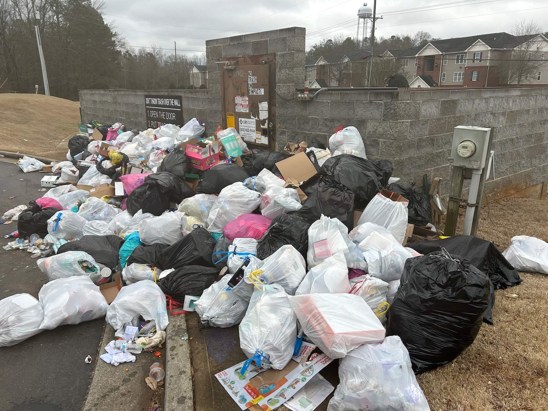 Overflowing piles of trash bags and litter piled against a stone wall on a street