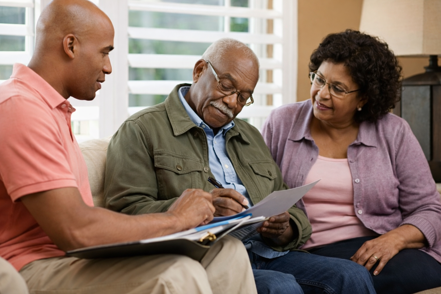 A person sits with an older couple as they review documents together in a brightly lit room.