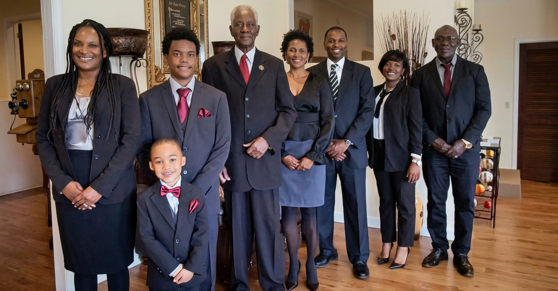 A group of eight people dressed in formal business attire pose together for a portrait in a well-lit interior space.