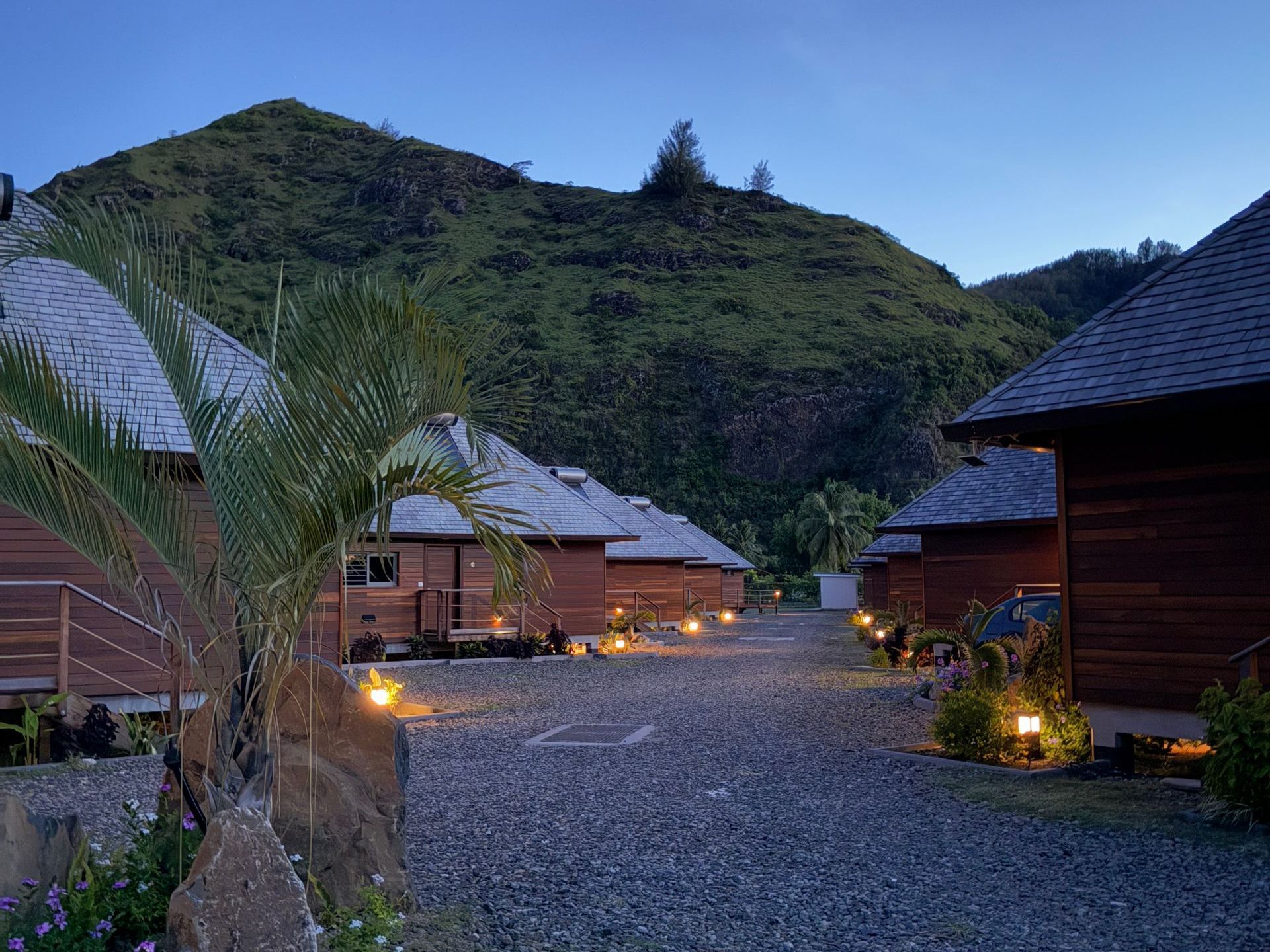 Wooden cabins with lighted pathways at dusk, mountain backdrop.