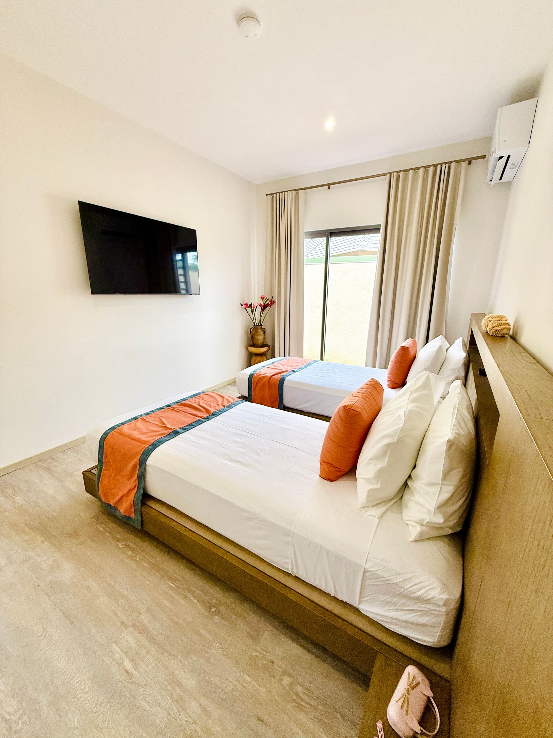 Bedroom with two beds, white linens, orange pillows, and a wall-mounted TV.