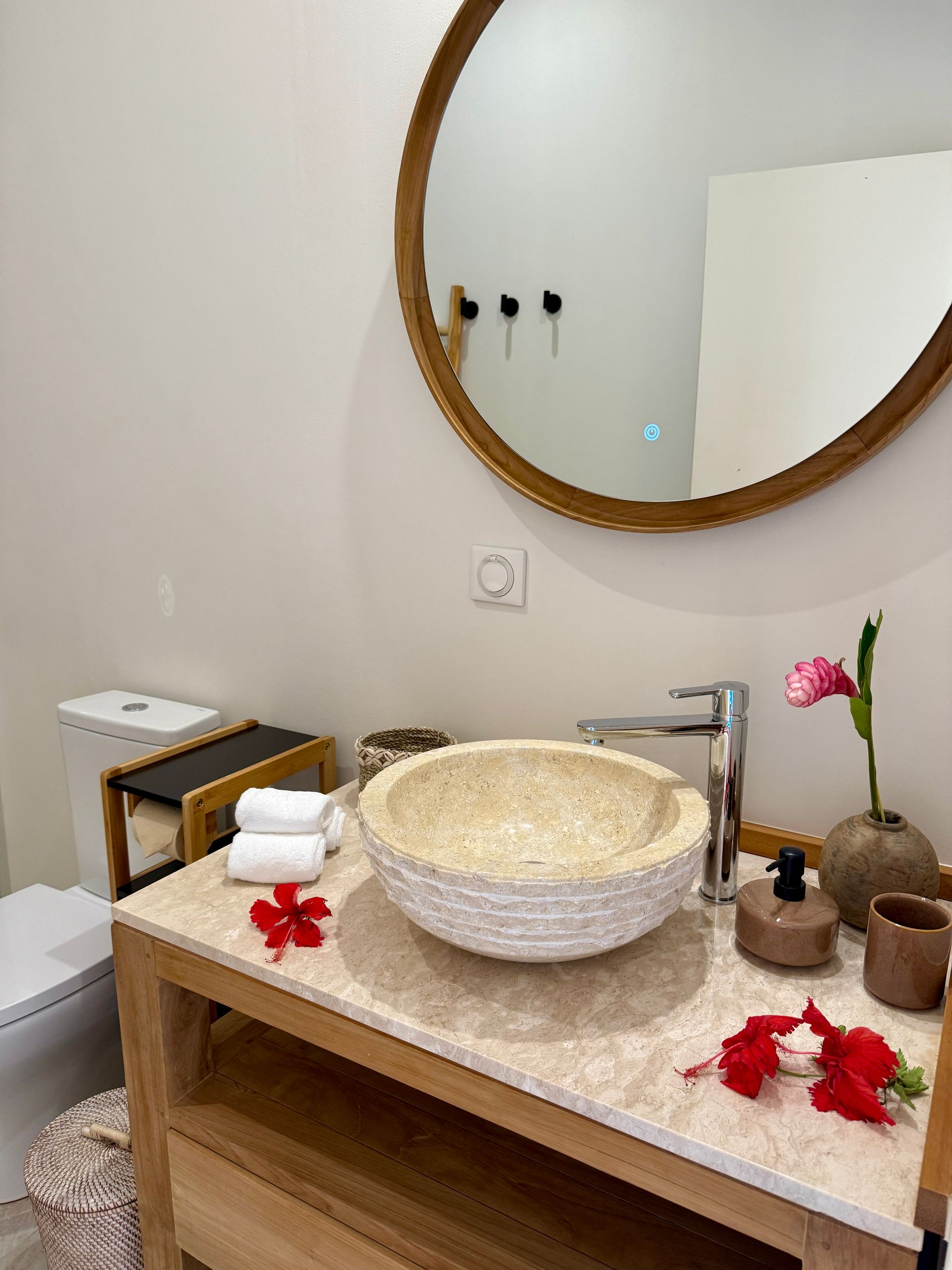 Bathroom with round mirror, stone sink, wooden vanity, and decorative flowers.