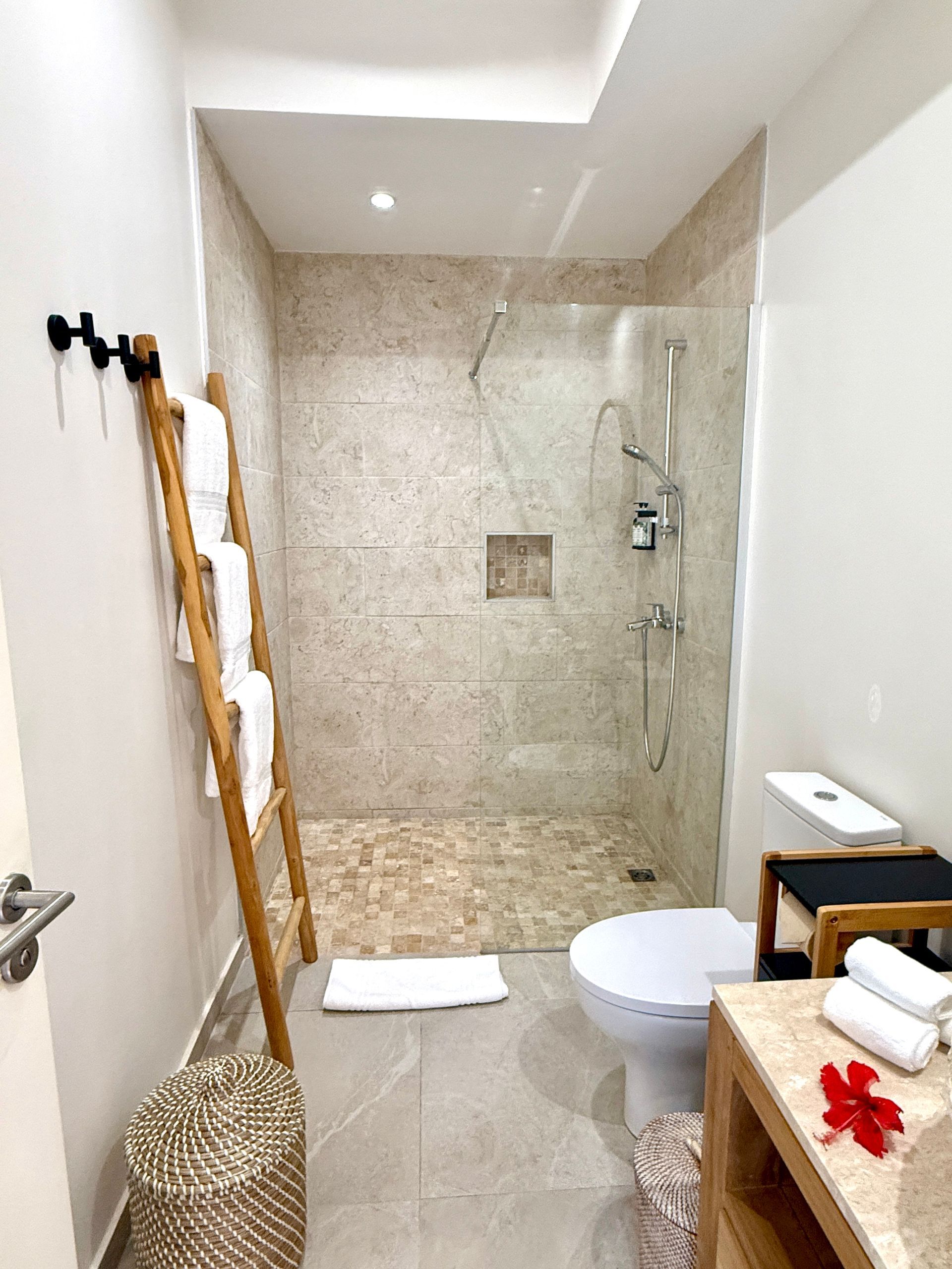 Bathroom with a walk-in shower, toilet, wooden ladder for towels, and a wicker basket. Neutral colors dominate.