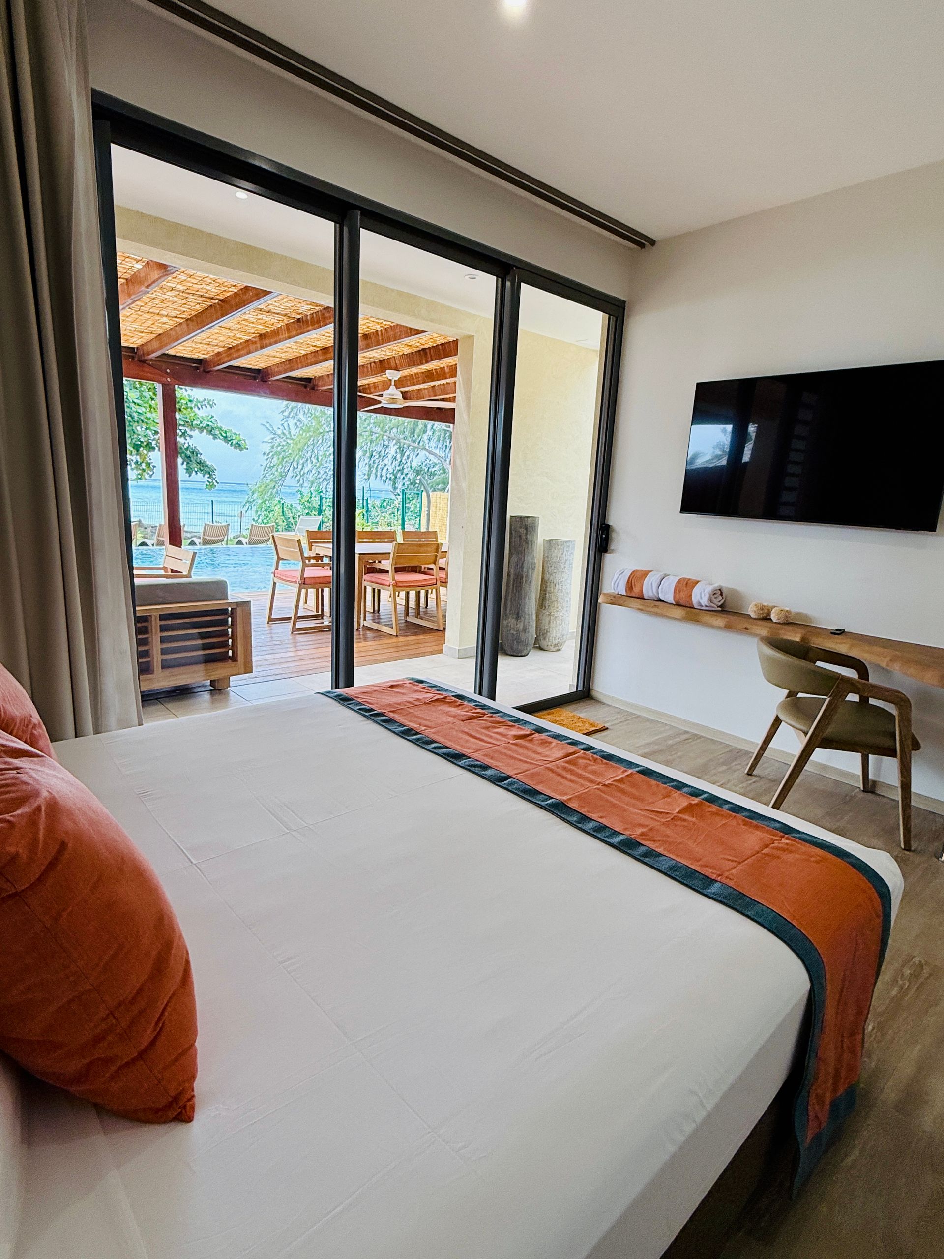 Bedroom with bed, desk, and sliding door to patio overlooking water.