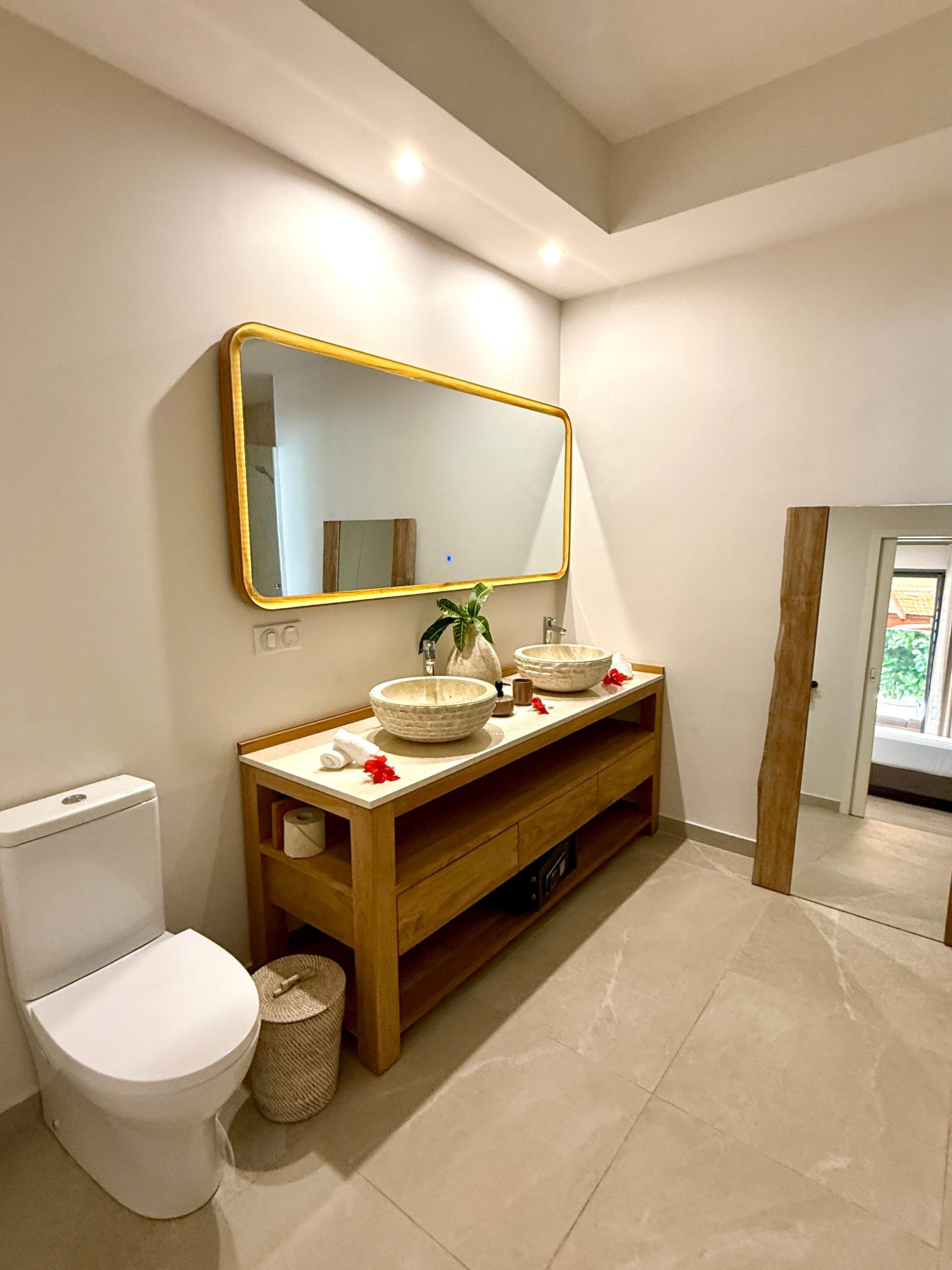Bathroom with wood vanity, large gold-framed mirror, and two sinks. Toilet on left.