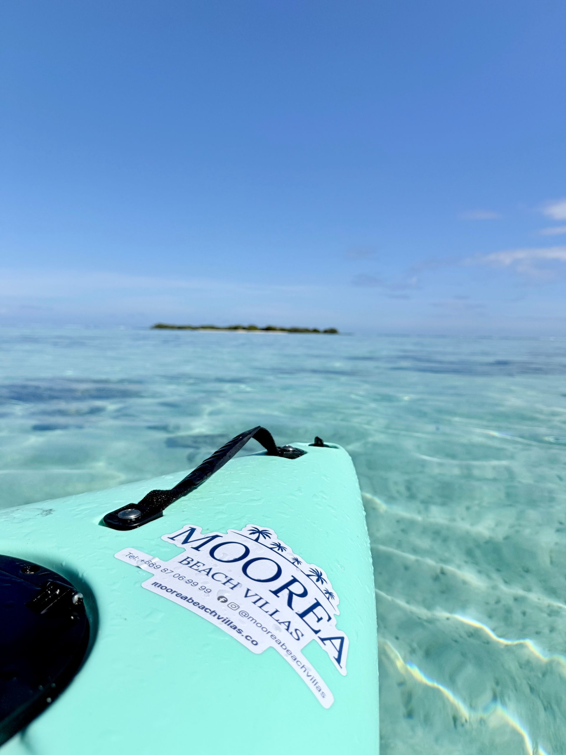 Teal kayak on clear water, distant island under blue sky.