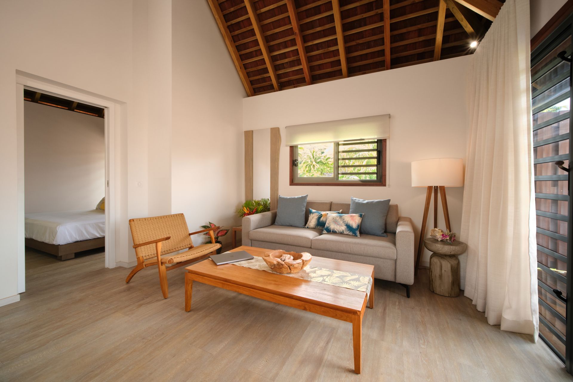 Bright living room with couch, wooden chair, table, and bedroom entrance.
