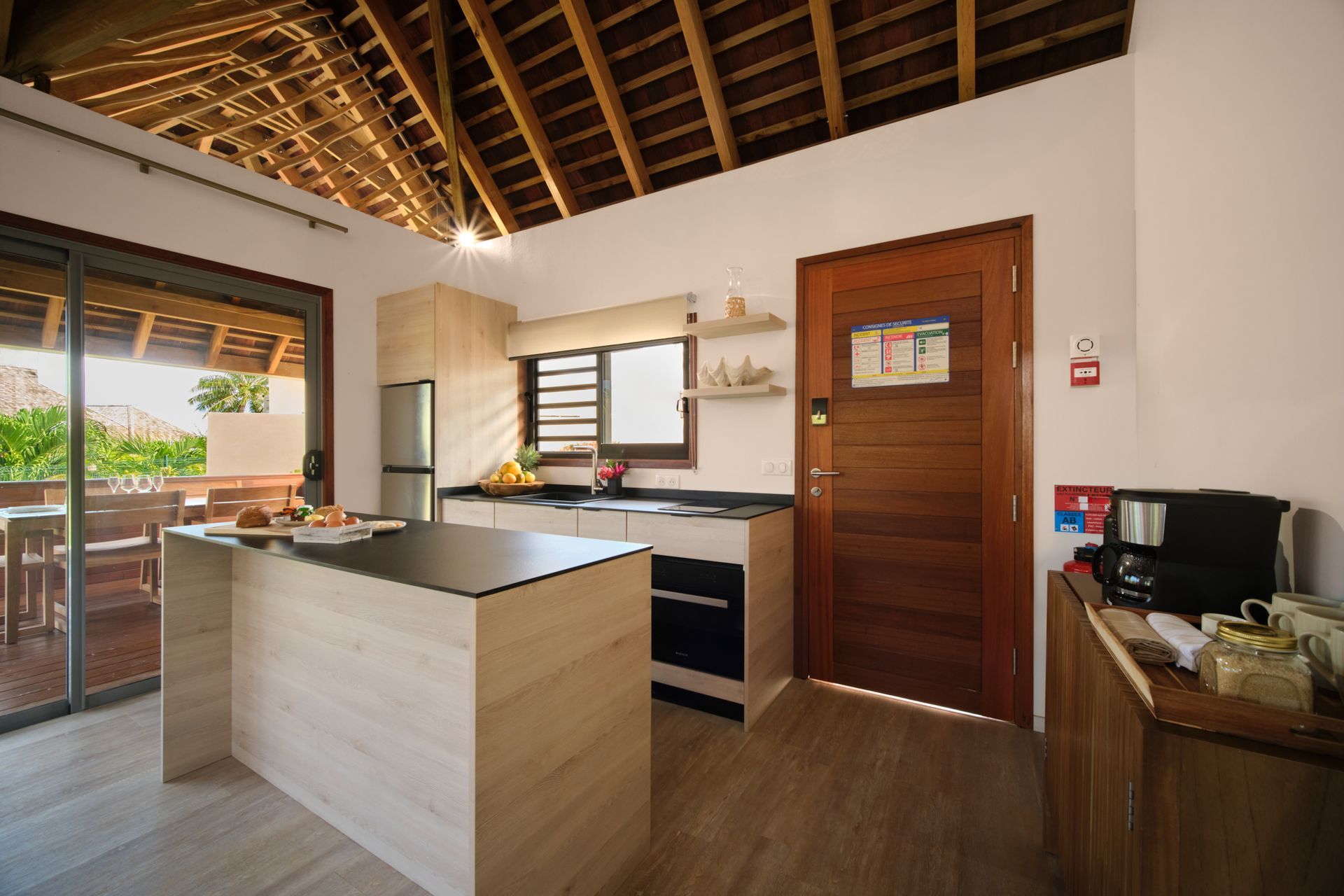 Bright kitchen with wooden beams, light wood cabinets, and an island. A sliding glass door leads to a deck.