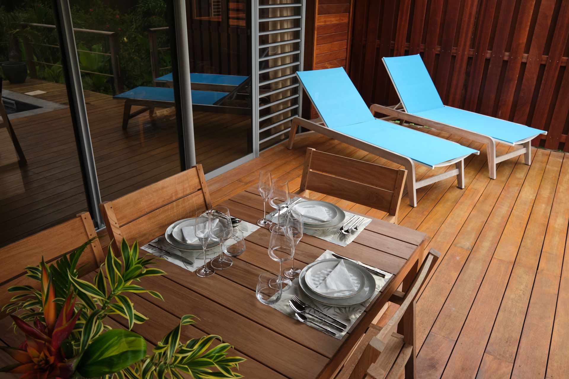 Outdoor deck with dining table set for two, and two turquoise chaise lounges.