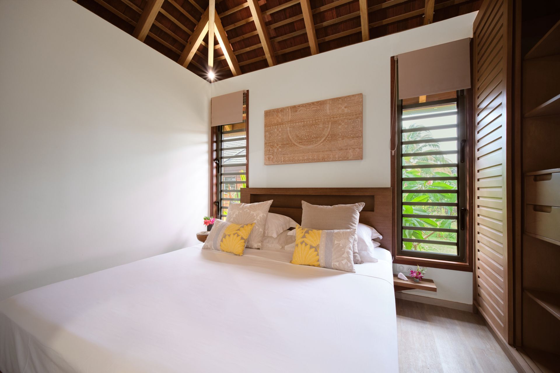 Bedroom with white walls, wooden ceiling and closet, double bed with pillows.