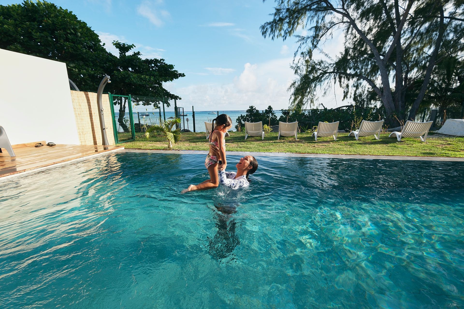 Person holding a child in a swimming pool, blue water, sunny day.