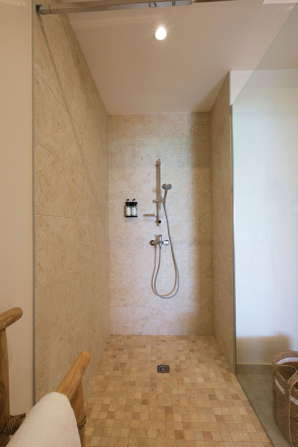 Walk-in shower with stone tile walls and floor. Chrome shower fixtures. Clear glass door on right.