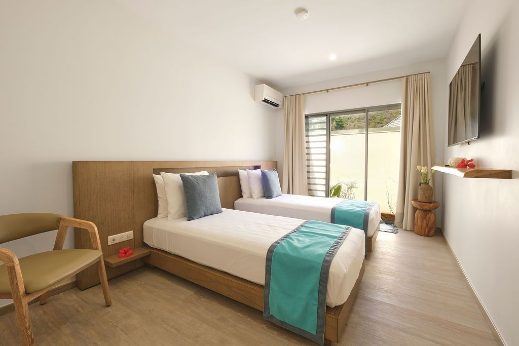 Bedroom with two twin beds, turquoise accents, wood headboard, chair, and a window.