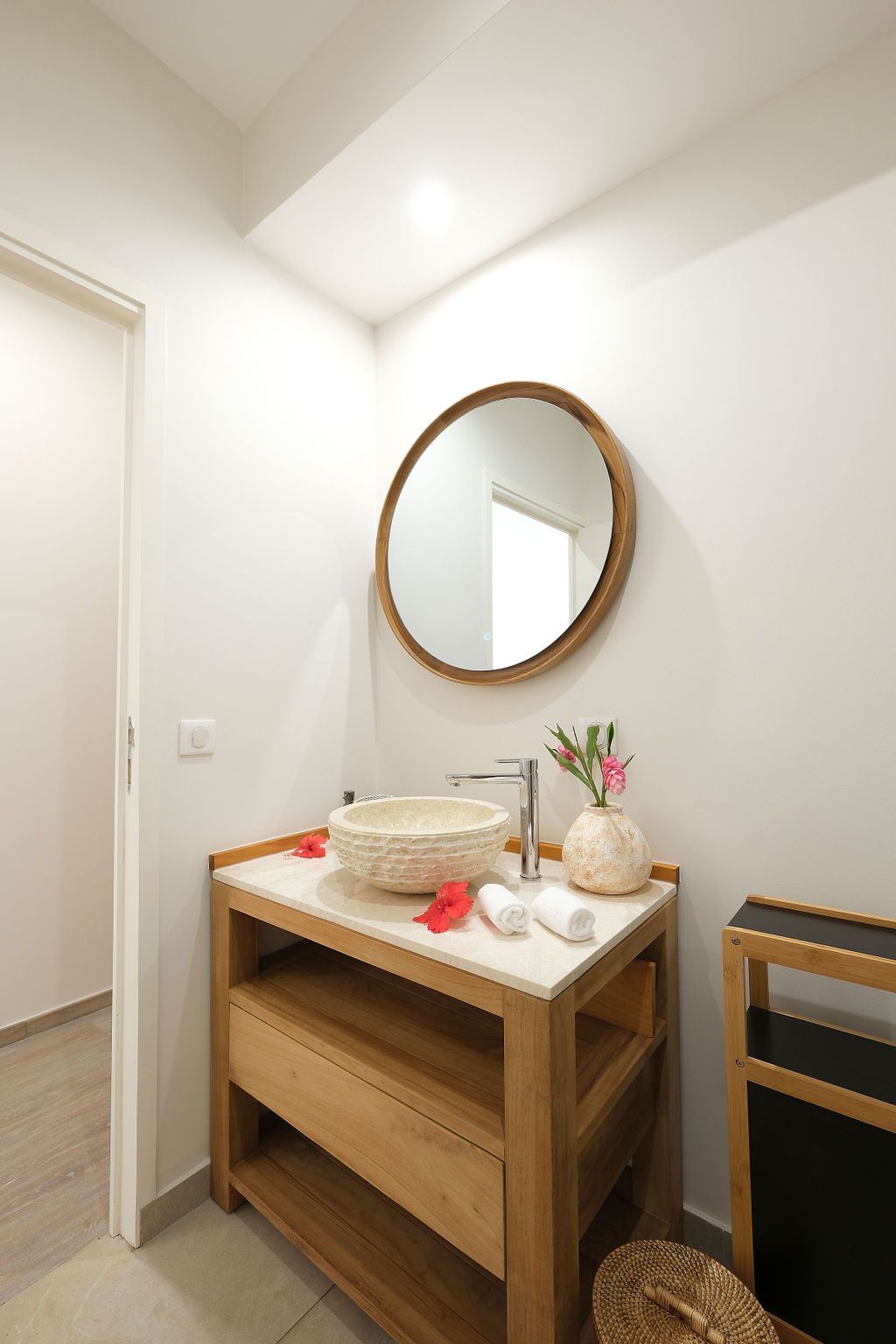 Bathroom with wooden vanity, round mirror, and stone sink; towels and flowers on the countertop.