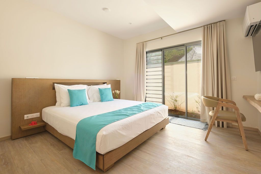 Bedroom with bed, blue accents, large window, and wooden chair.