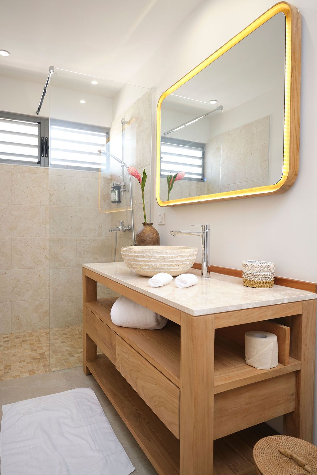 Bathroom with wood vanity, marble top, large gold-framed mirror, and shower with stone flooring.