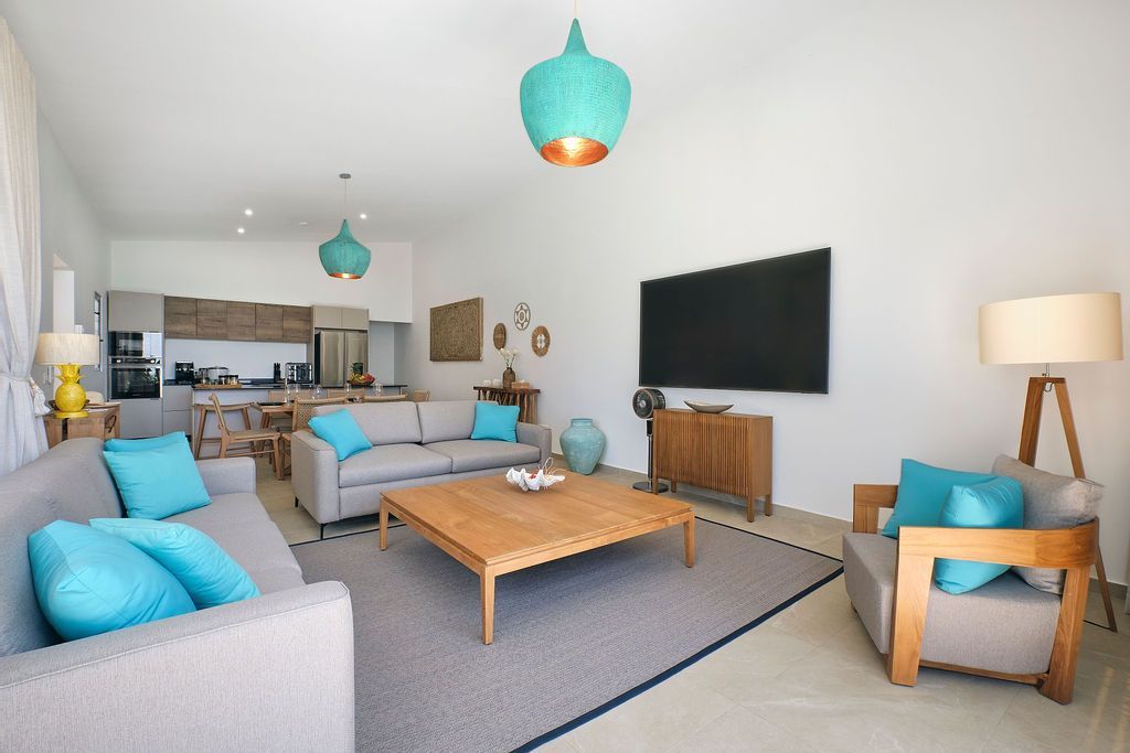 Spacious living room with gray sofas, wooden furniture, turquoise accents, and a large TV.