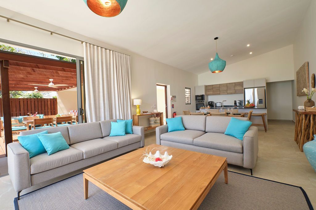 Spacious living room with light gray sofas, turquoise pillows, a wooden coffee table, and open doors to an outdoor patio.