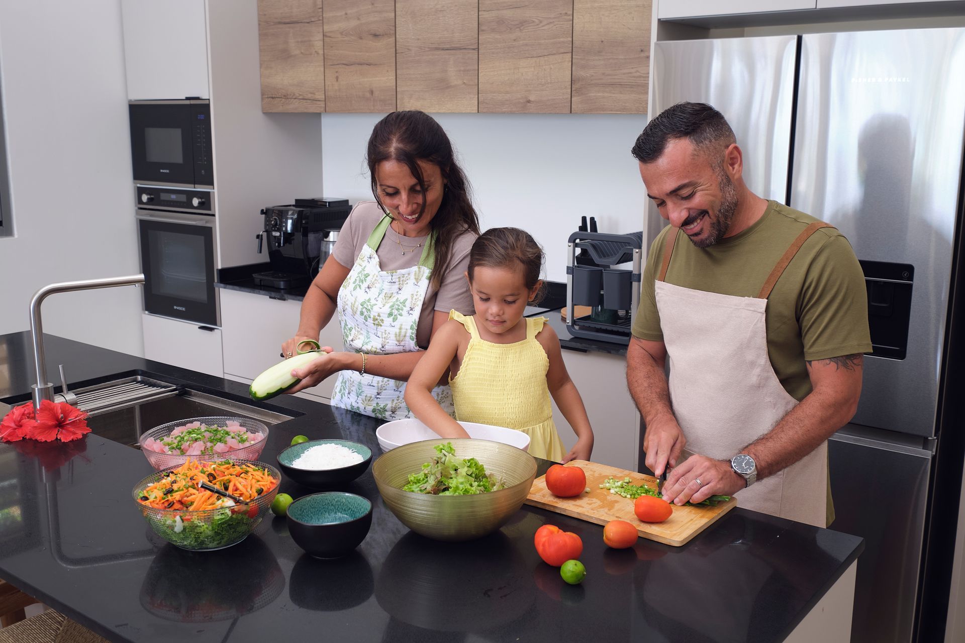 Family preparing food together in a kitchen. They are smiling and working at a counter with bowls of food.