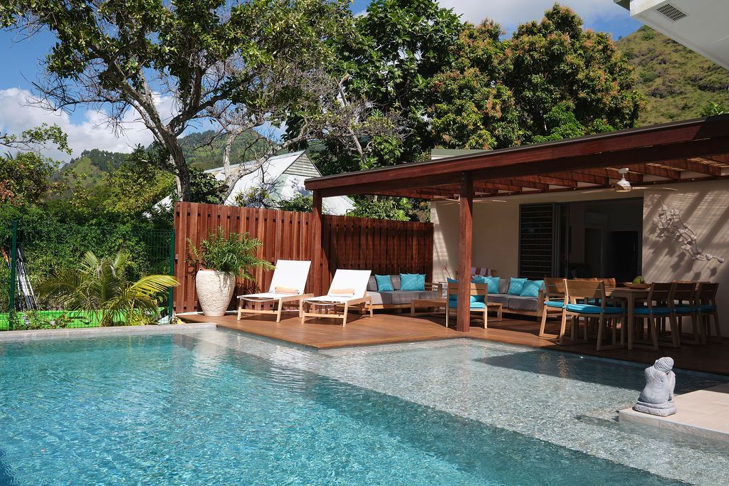 Swimming pool with deck area, lounge chairs, dining table, and greenery. Mountain background.