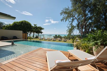 Swimming pool with wooden deck, sun loungers, and ocean view on a sunny day.