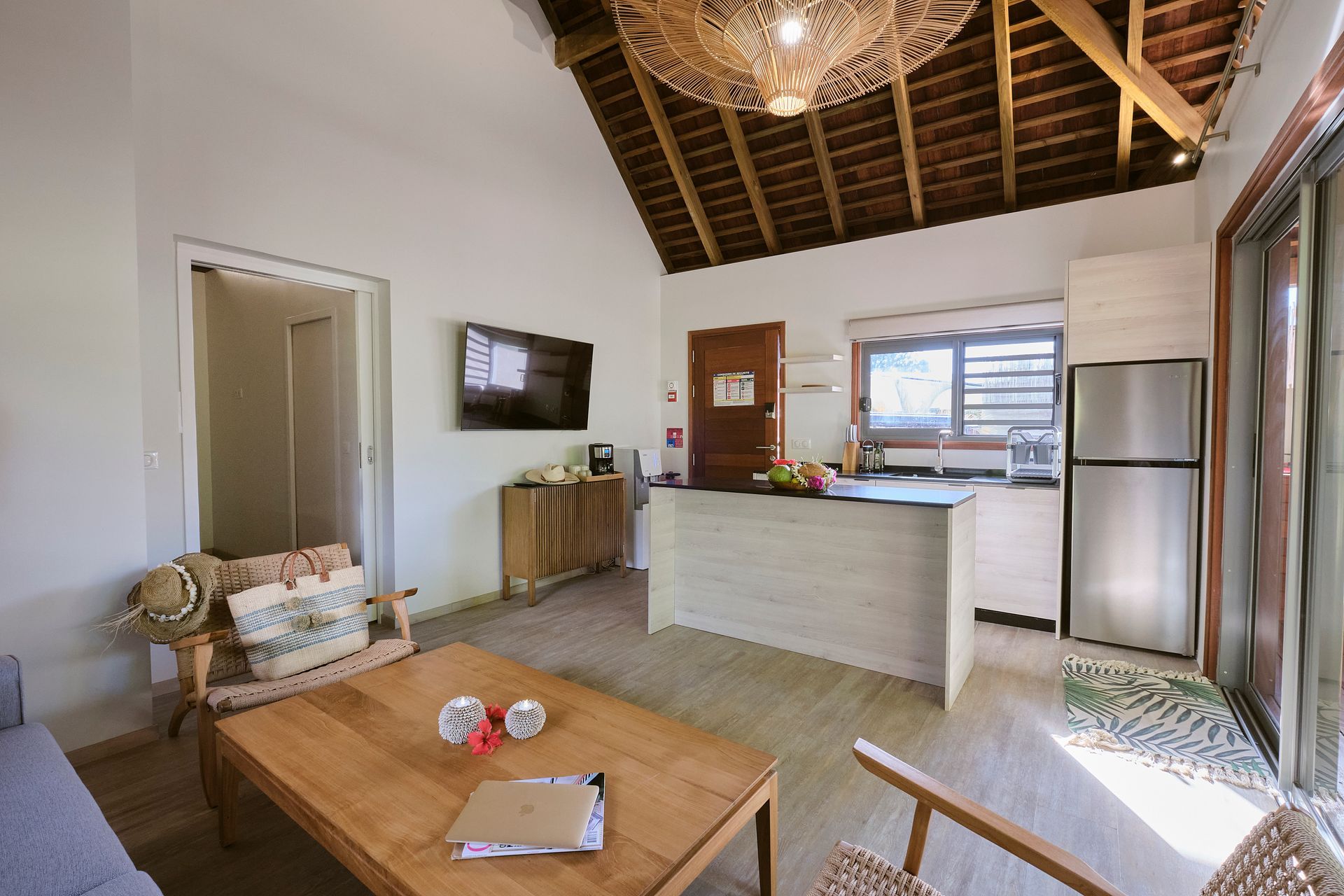 Living area with wooden furniture, small kitchen, vaulted ceiling, and sliding glass door.
