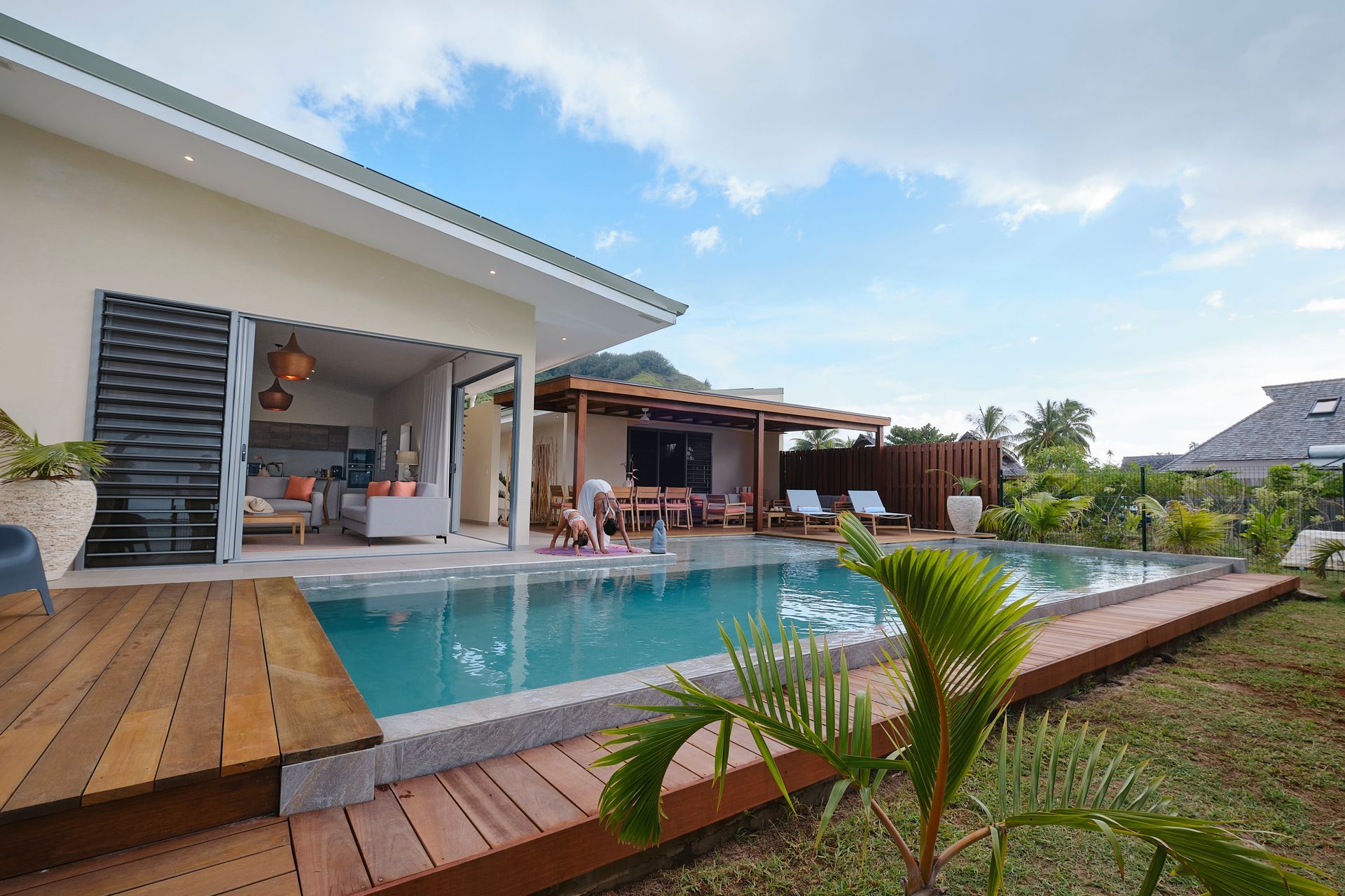 Poolside villa with pool and outdoor dining area; sunny day.