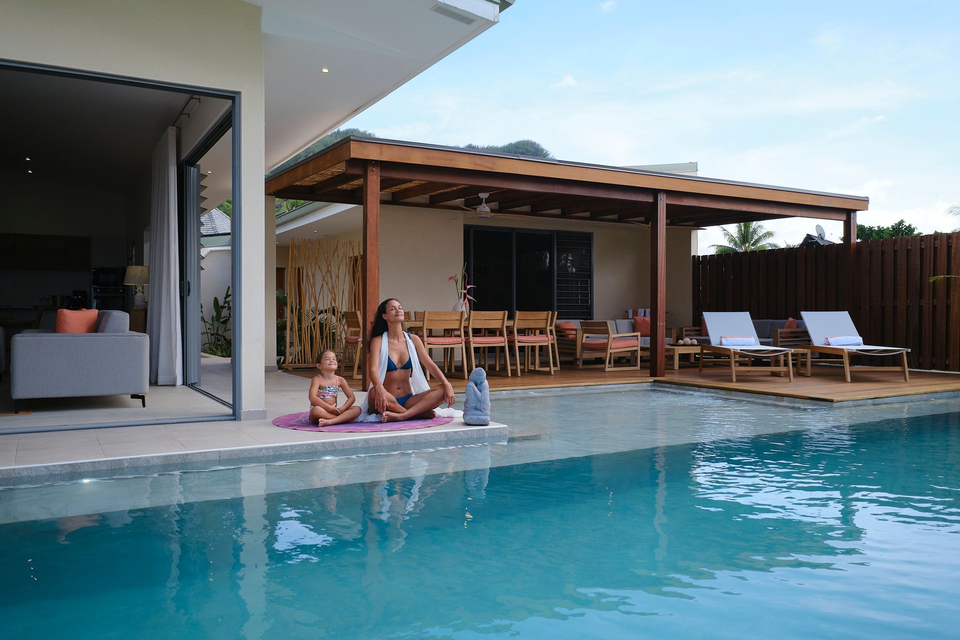 Woman and child sit near a pool; the woman is in swimwear.