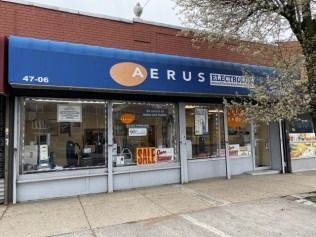 Storefront with blue awning and “Aerus Electrolux” sign, sale posters in the windows.