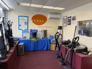 Gym showroom with exercise machines and blue-covered display tables under an orange Electrolux sign