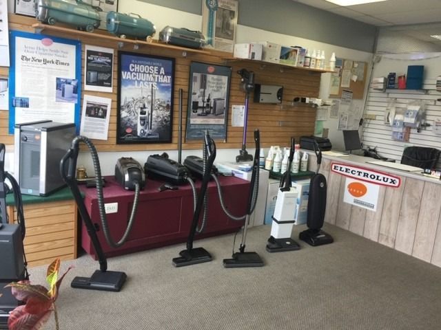 Vacuum cleaners lined up in a carpet cleaning shop with posters and equipment shelves.