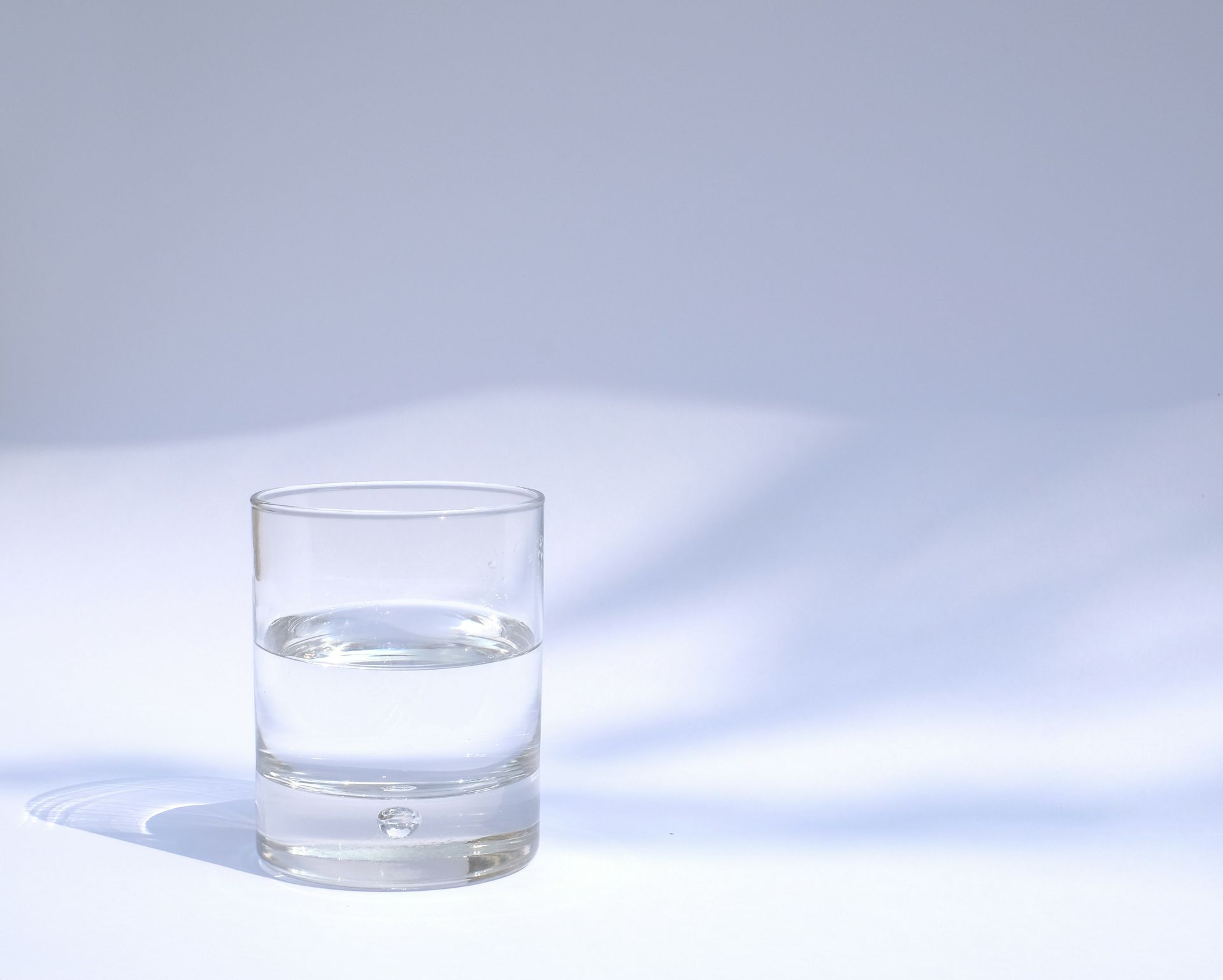 Clear glass of water on a white surface with a soft blue shadow